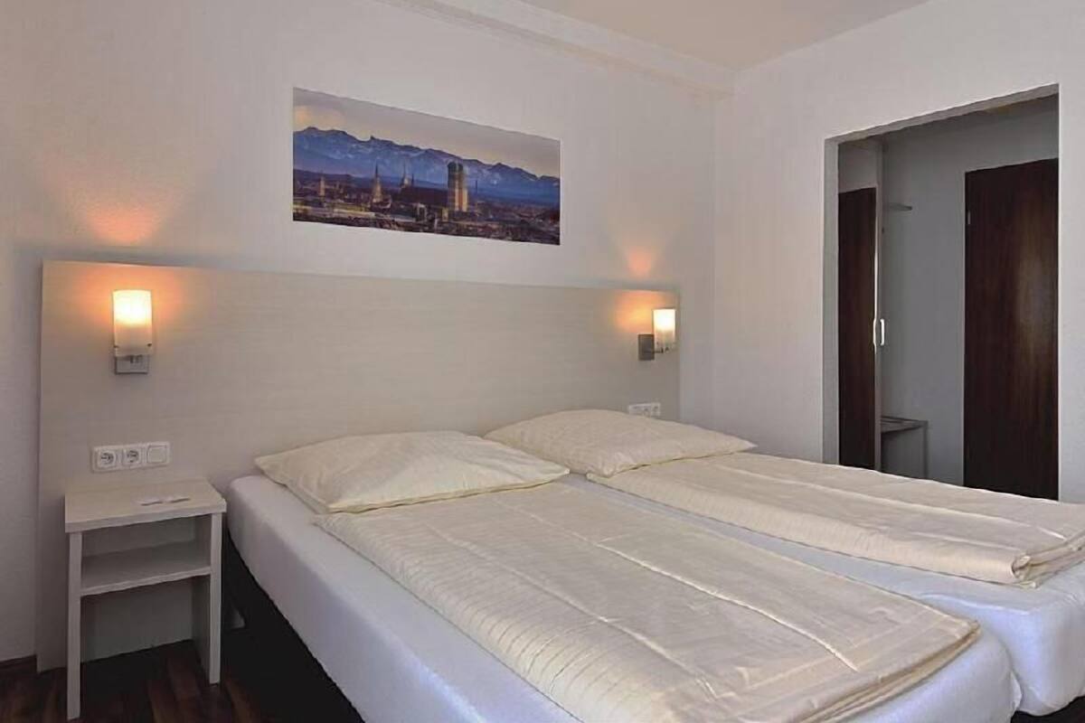 A hotel room with two beds, a nightstand, a wall-mounted picture, and a door leading to another room.