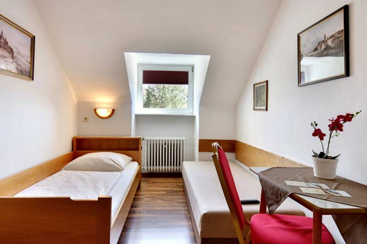A small, cozy room with two single beds, a bench, a table with a potted plant, and a window with a view.