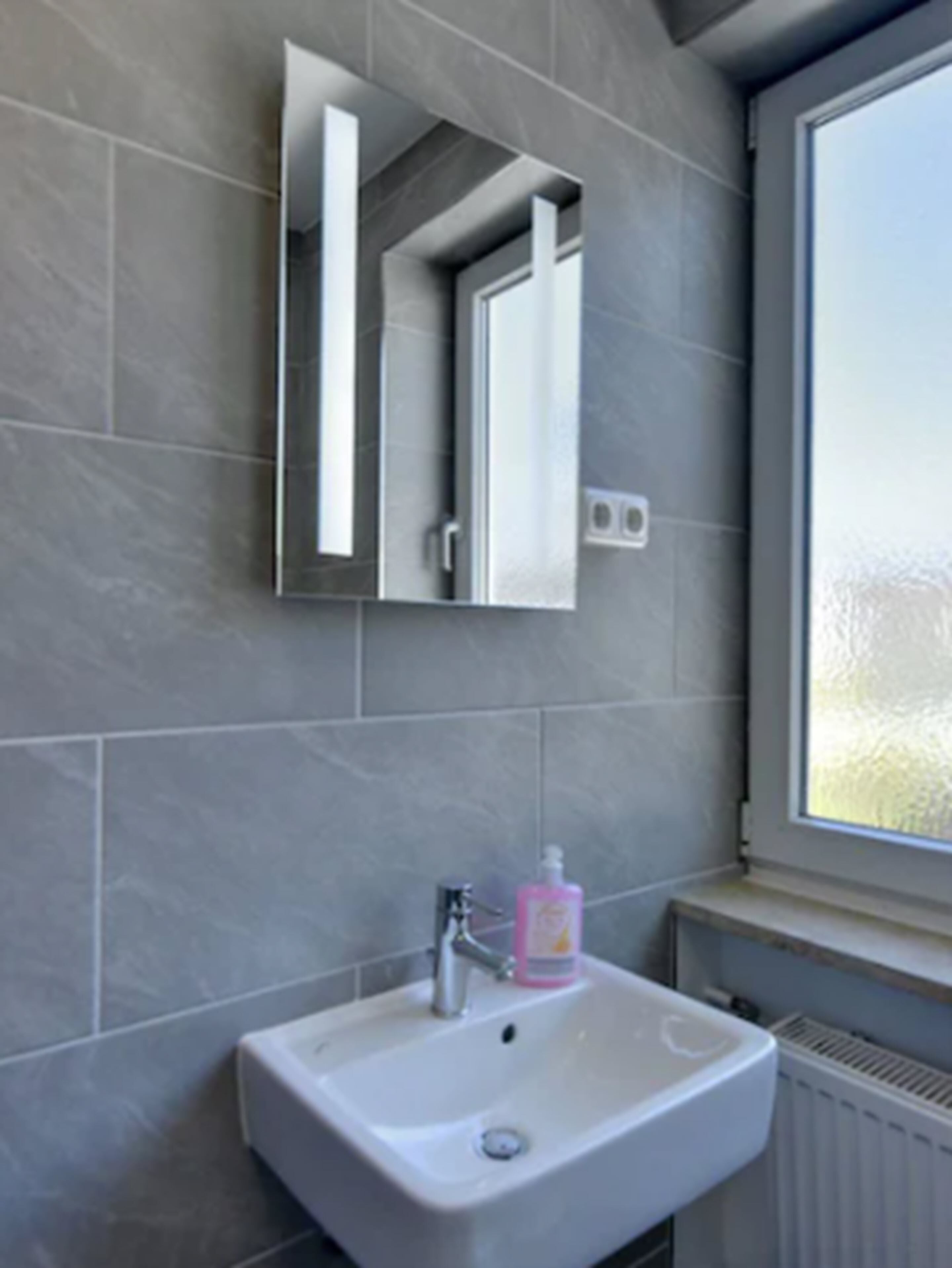 Une salle de bain avec un lavabo blanc, un miroir et une fenêtre.