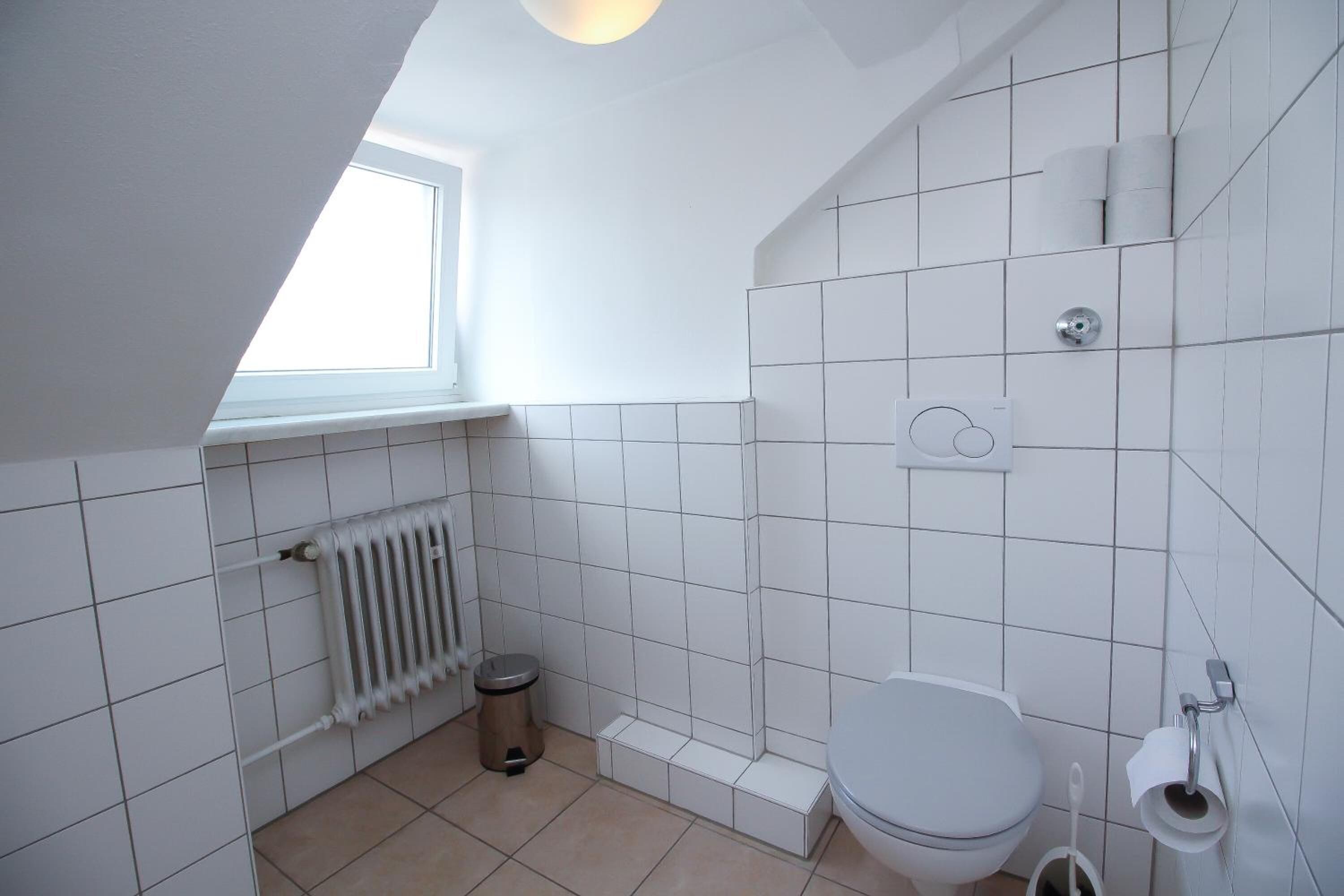 A small, white bathroom with a radiator, a toilet, and a window.