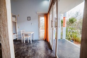 A room with a table and chairs, a door leading outside, and a view of greenery. - Lemon Hostel Lembongan (Lembongan Island)