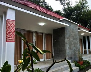 A building with a red-tiled roof, a stone wall, and a covered entrance with a patterned fabric. - Lemon Hostel Lembongan (Lembongan Island)
