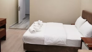 Quarto de hotel moderno com uma cama grande, mesas de cabeceira e um banco de madeira.