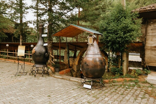 Two large metal containers with stands, set on a paved area with trees and a wooden structure in the background. - Sumela Holiday Hotel (Maçka)