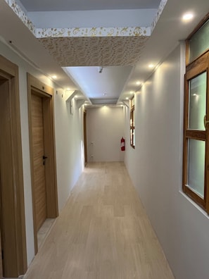 Un pasillo con puertas de madera, un extintor y luces empotradas en el techo.