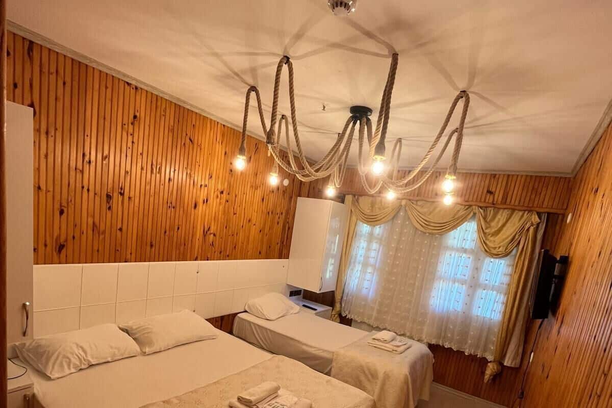 A hotel room with two beds, a wooden wall, a chandelier, and a television.