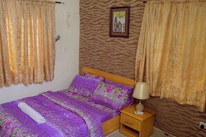 A bedroom with a bed, curtains, a nightstand, a lamp, and a wall with a patterned wallpaper.
