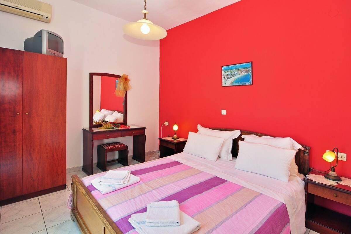Quarto com cama, mesas de cabeceira, cômoda, espelho e ar-condicionado fixado na parede.