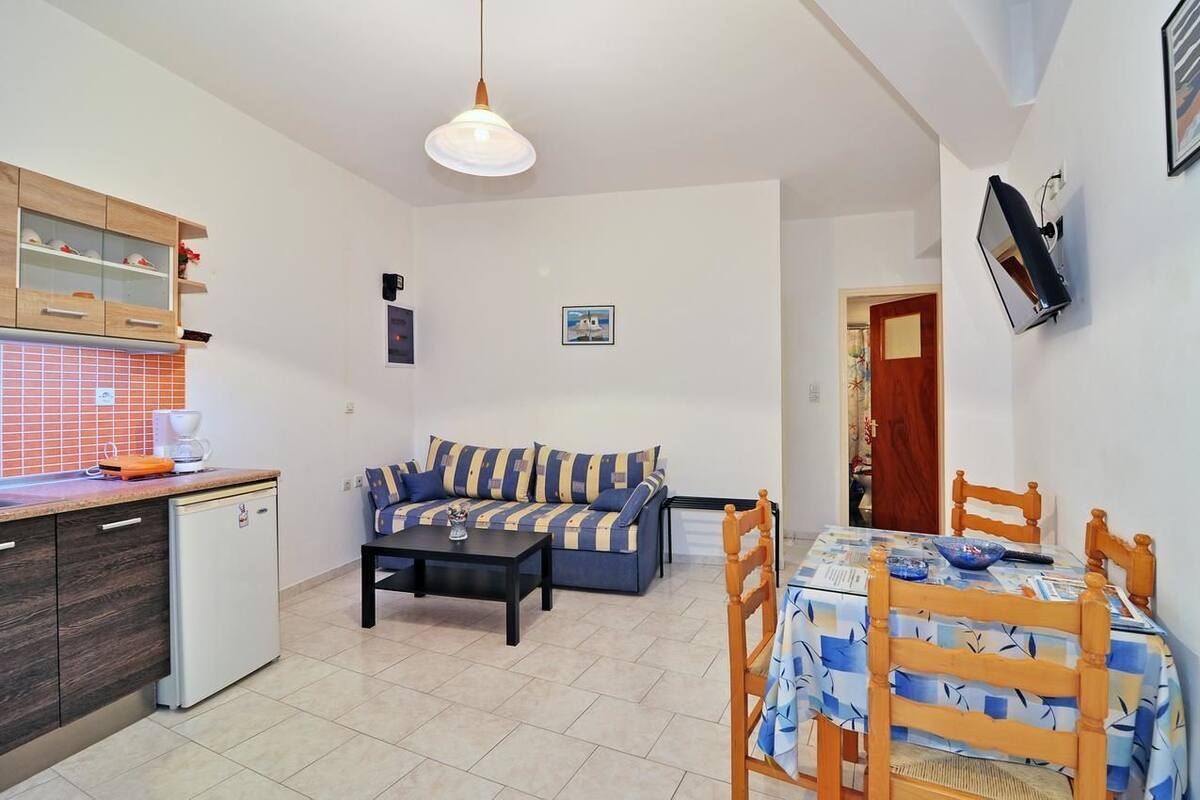 Um espaço compacto com cozinha compacta, sofá, mesa de jantar e um frigorífico pequeno.