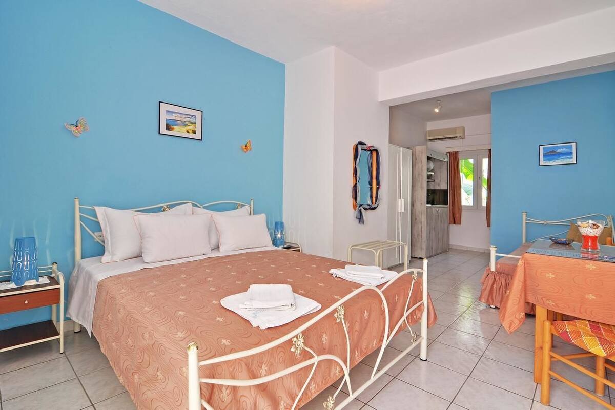 Quarto com cama, mesa de cabeceira e vista para a cozinha.