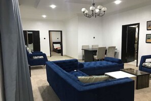 A modern living room with a blue sofa set, a coffee table, and a dining area with chairs and a table. - Perfect Havens (Lagos)