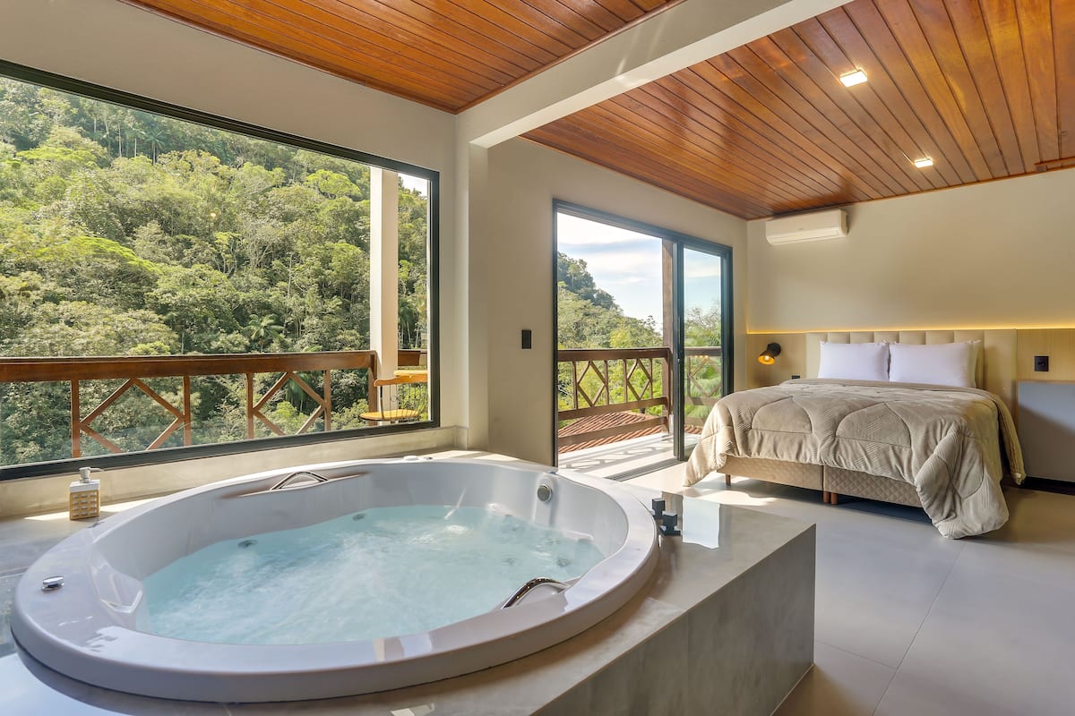 A modern bedroom with a large window, a hot tub, and a bed with a headboard.