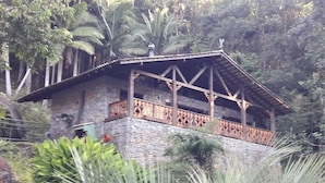 A stone building with a wooden balcony, surrounded by lush greenery. - Pousada Alpenhof (Sao Pedro de Alcantara)