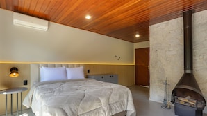 A modern bedroom with a large bed, a stone wall, and a wood-burning stove. - Pousada Alpenhof (Sao Pedro de Alcantara)