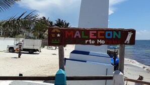 A lighthouse with a sign reading "MALECON De Puerto Morelos" on a beach with palm trees and a truck in the background. - Casa Falabella - Puerto Marino (Puerto Morelos)