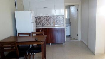 A compact kitchen with a dining table and chairs, a refrigerator, and a tiled backsplash.