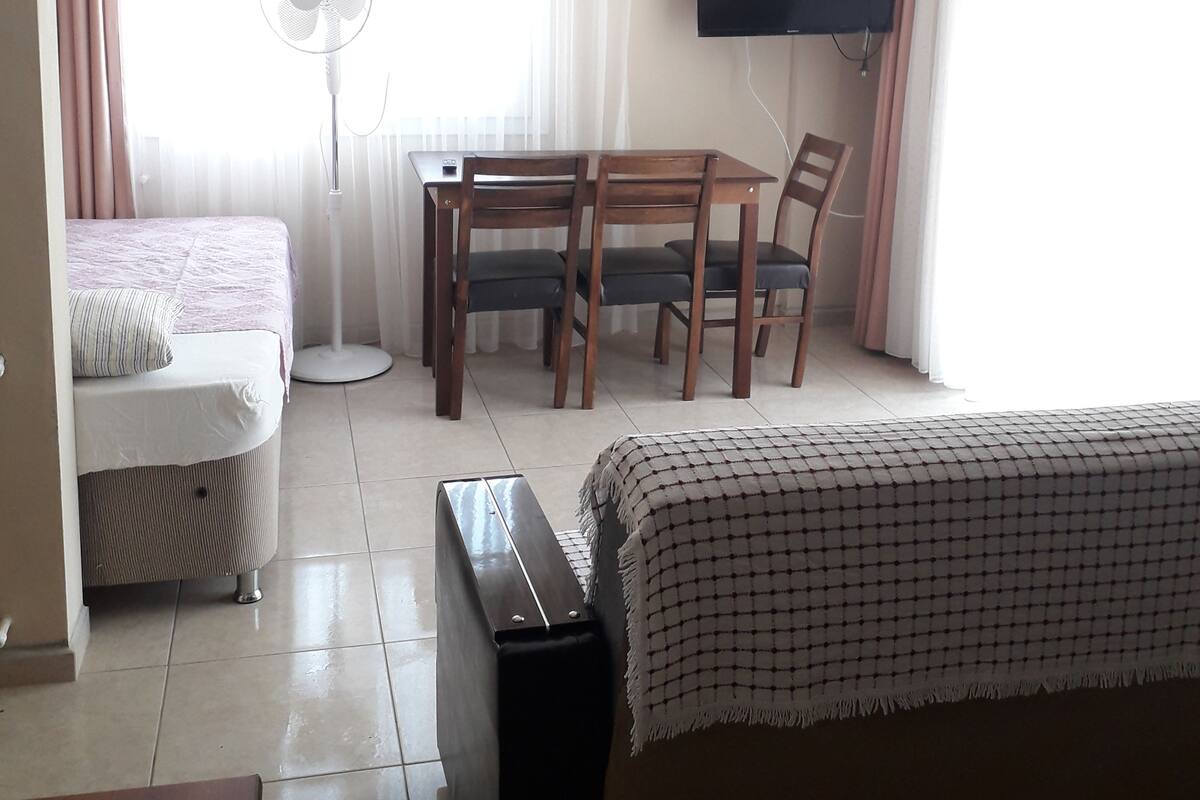 Ein Hotelzimmer mit Bett, Schreibtisch mit Stuhl, Wandfernseher und Standventilator.