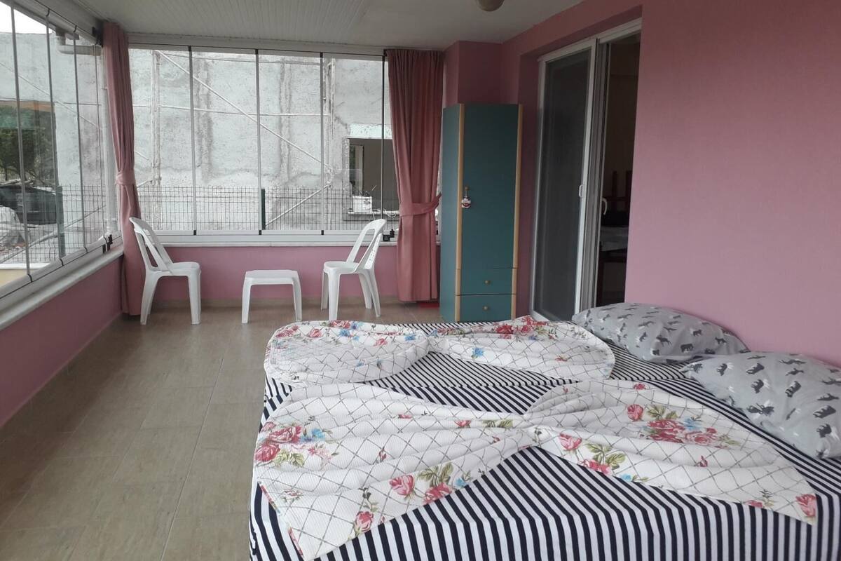 Ein Zimmer mit einem Bett, zwei Stühlen, einem Kleiderschrank und einem Fenster mit Blick auf ein Gebäude.