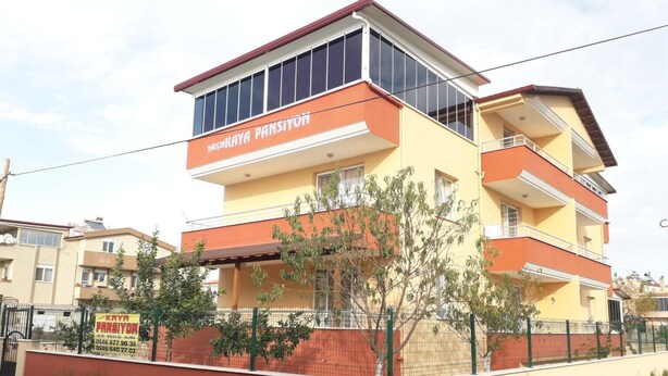 A multi-story building with a yellow facade and orange accents, featuring balconies and large windows. - Yalcinkaya Pansiyon (Burhaniye)