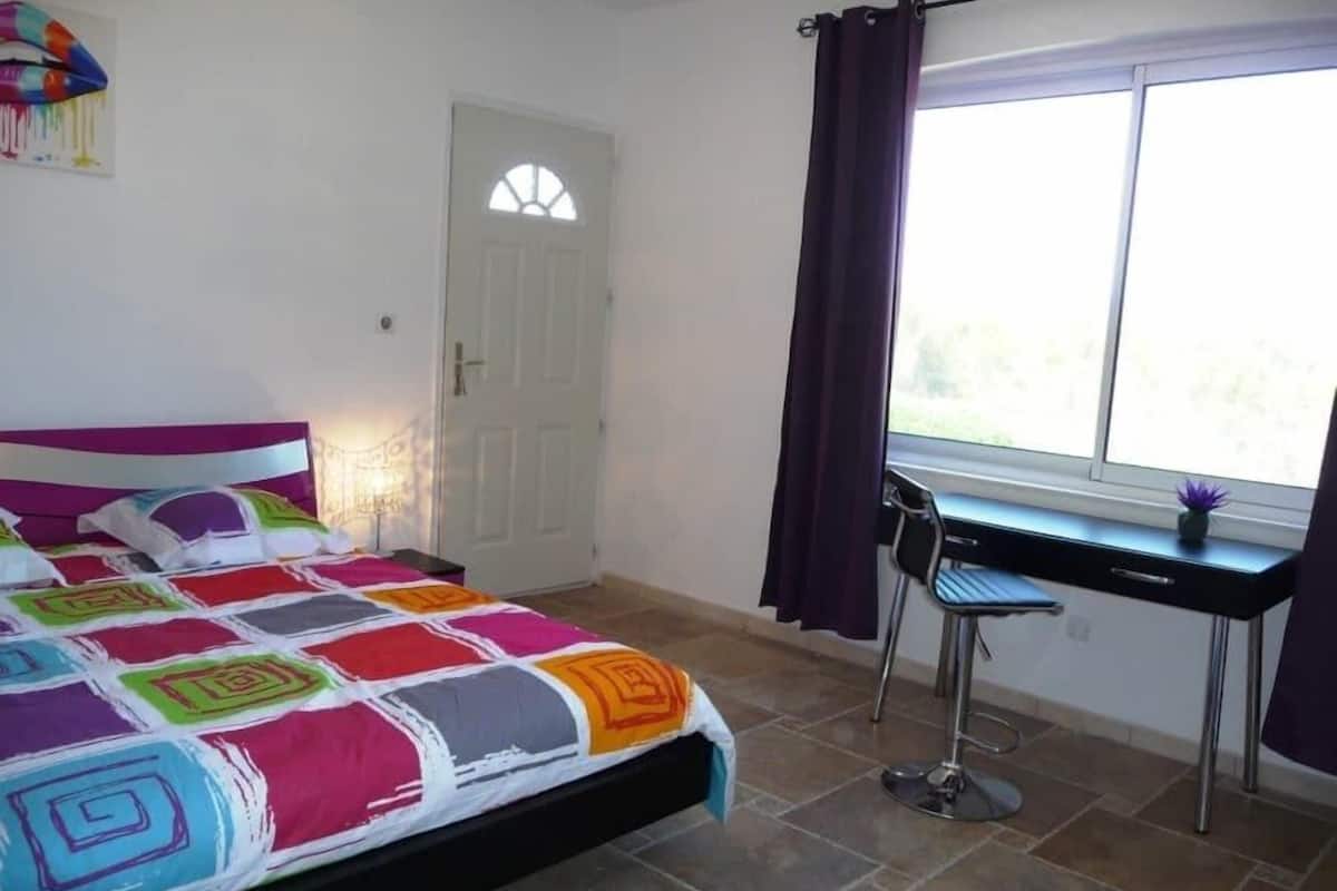 A bedroom with a bed, a desk, and a window.
