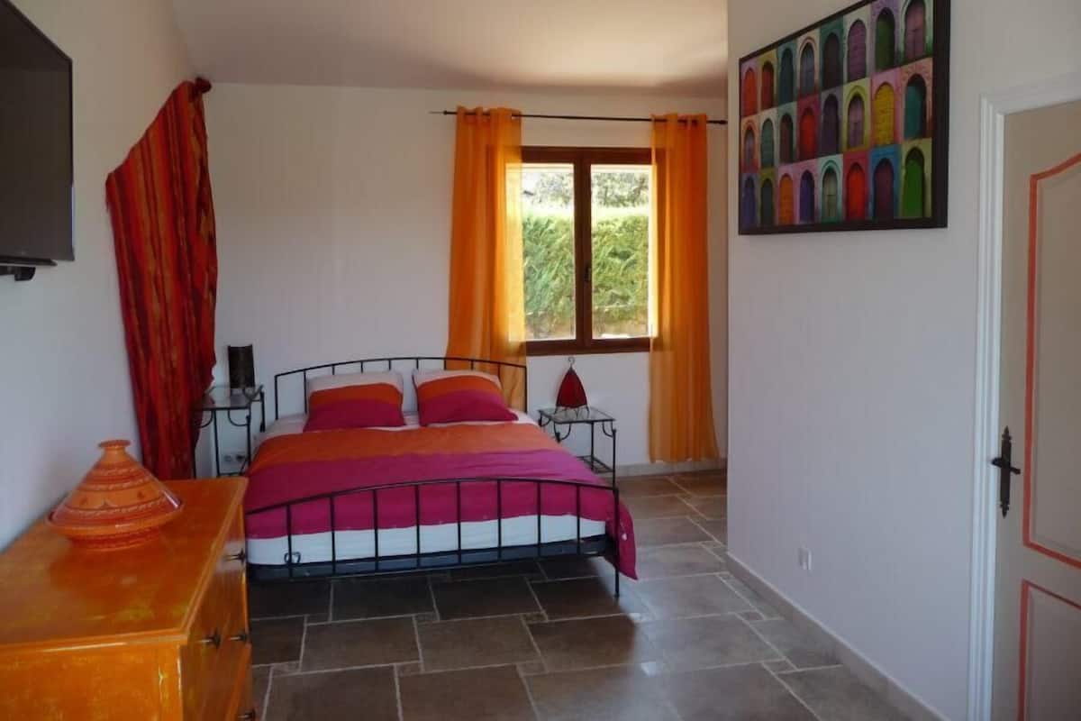 A bedroom with a bed, curtains, a painting, and a door.