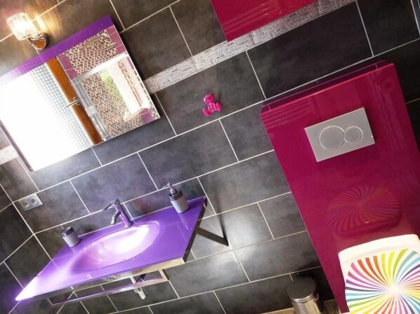 Un baño con un lavamanos morado, un espejo y una pared rosa.