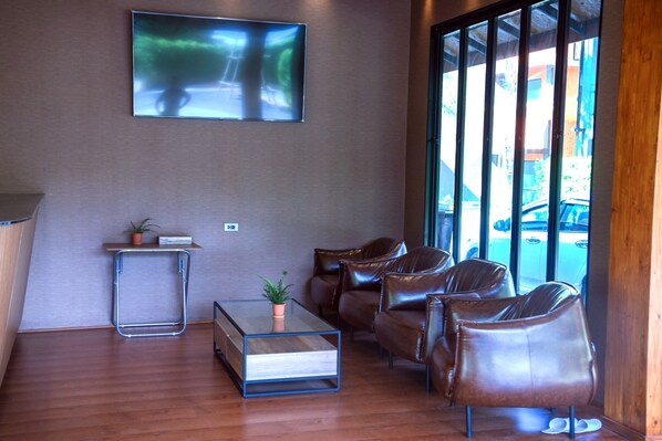 Un vestíbulo moderno con sillones de cuero, una mesa de centro de vidrio y un televisor de pantalla plana en la pared.