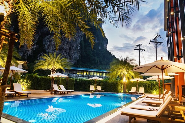 A swimming pool with lounge chairs and umbrellas, surrounded by greenery and a building with a view of a cliff. - Frank Ao Nang Krabi Resort (Krabi)