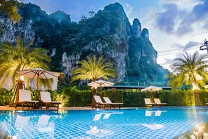 A swimming pool with lounge chairs and umbrellas, surrounded by lush greenery and a mountainous backdrop. - Frank Ao Nang Krabi Resort (Krabi)