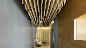 A corridor with a wooden floor, a wall with vertical bamboo-like structures, and a window on the right. - Pod Labo (Hualien City)