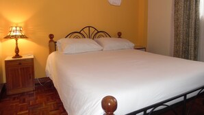 Una cama con ropa de cama blanca, una mesita de noche de madera con una lámpara y una mosquitera sobre la cama.