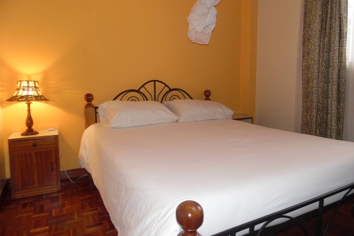 A bed with white bedding, a wooden nightstand with a lamp, and a mosquito net above the bed.