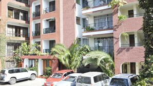 Un edificio residencial de varios pisos con balcones, coches aparcados y áreas verdes.