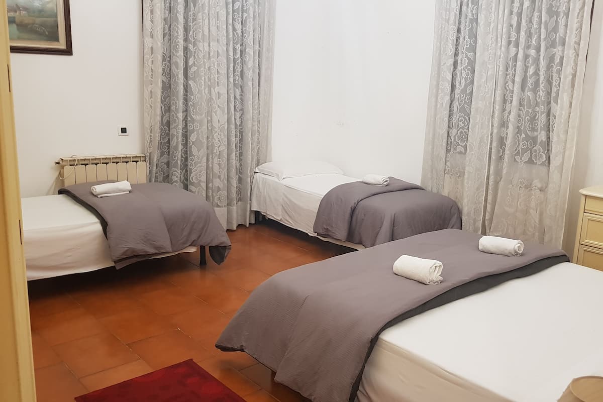 A hotel room with two single beds, a wooden floor, a radiator, and a small bedside table.