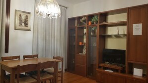 A dining area with a wooden table and chairs, a chandelier, and a cabinet with shelves and a television. - Venetian Style (Venice)