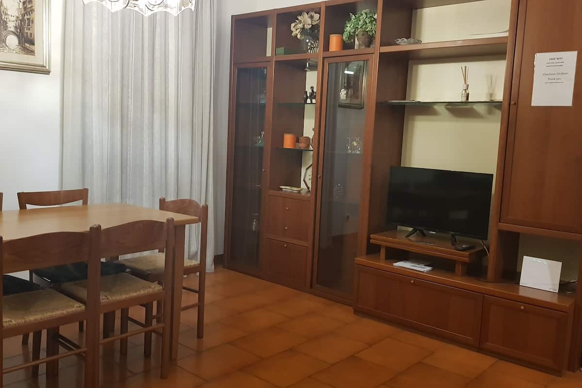 A dining area with a wooden table and chairs, a television on a wooden stand, and a cabinet with glass doors.