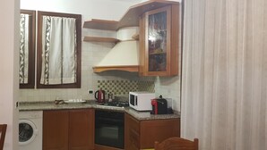 A compact kitchen with a washing machine, stove, microwave, and wooden cabinets. - Venetian Style (Venice)