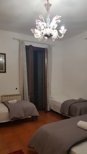 A room with two beds, a chandelier, a door, and a radiator. - Venetian Style (Venice)