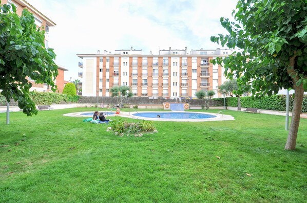 Un patio con piscina, rodeado de césped cuidado y árboles.