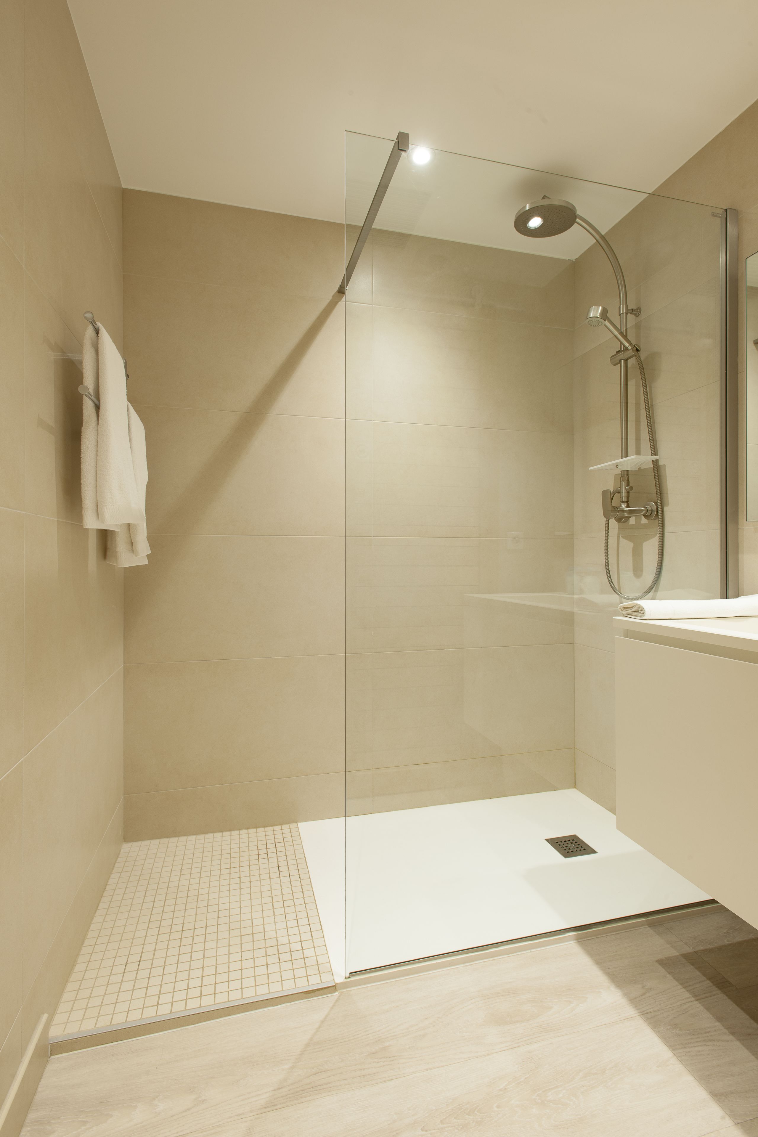 Un espacio de ducha moderno con puerta de cristal, un lavamanos blanco y una toalla colgada en la pared.