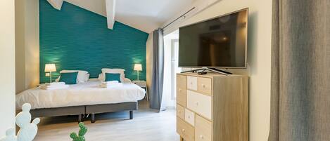 A modern hotel room with a bed, a TV, a dresser, and a small cactus on a table.