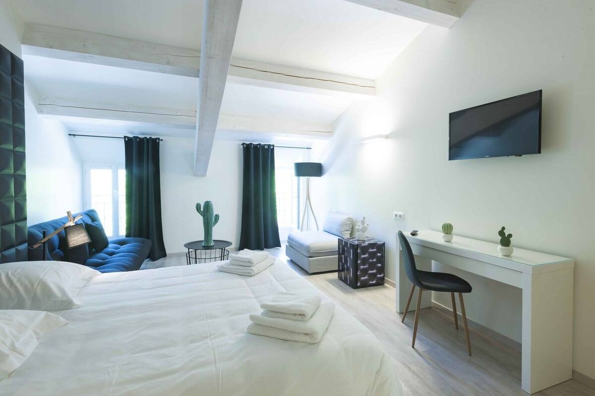 A modern hotel room with a large bed, a desk, a chair, a TV, and a cactus on the desk.