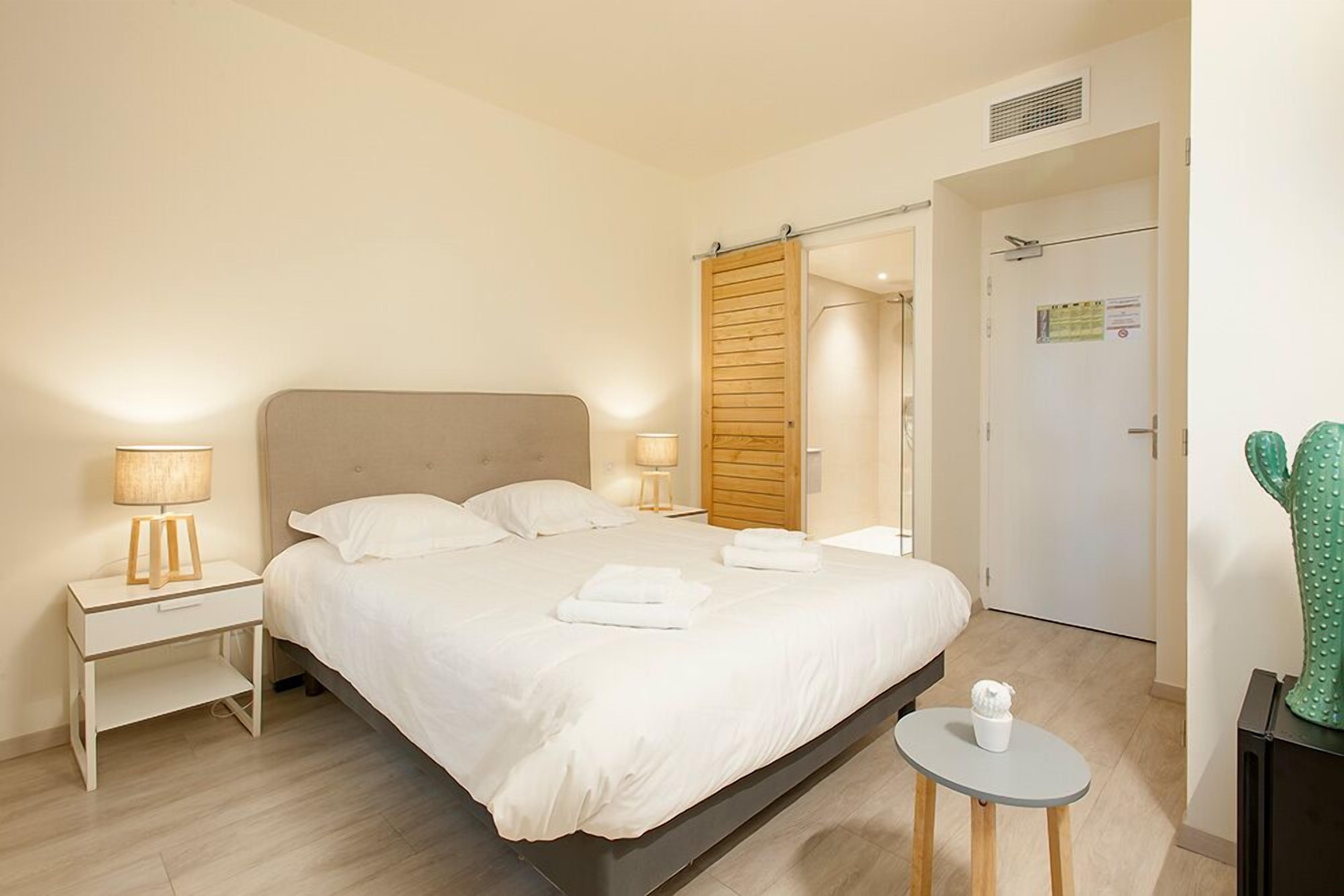 Ein modernes Hotelzimmer mit einem großen Bett, Nachttischlampen, einem kleinen Tisch und einer Kakteendekoration.
