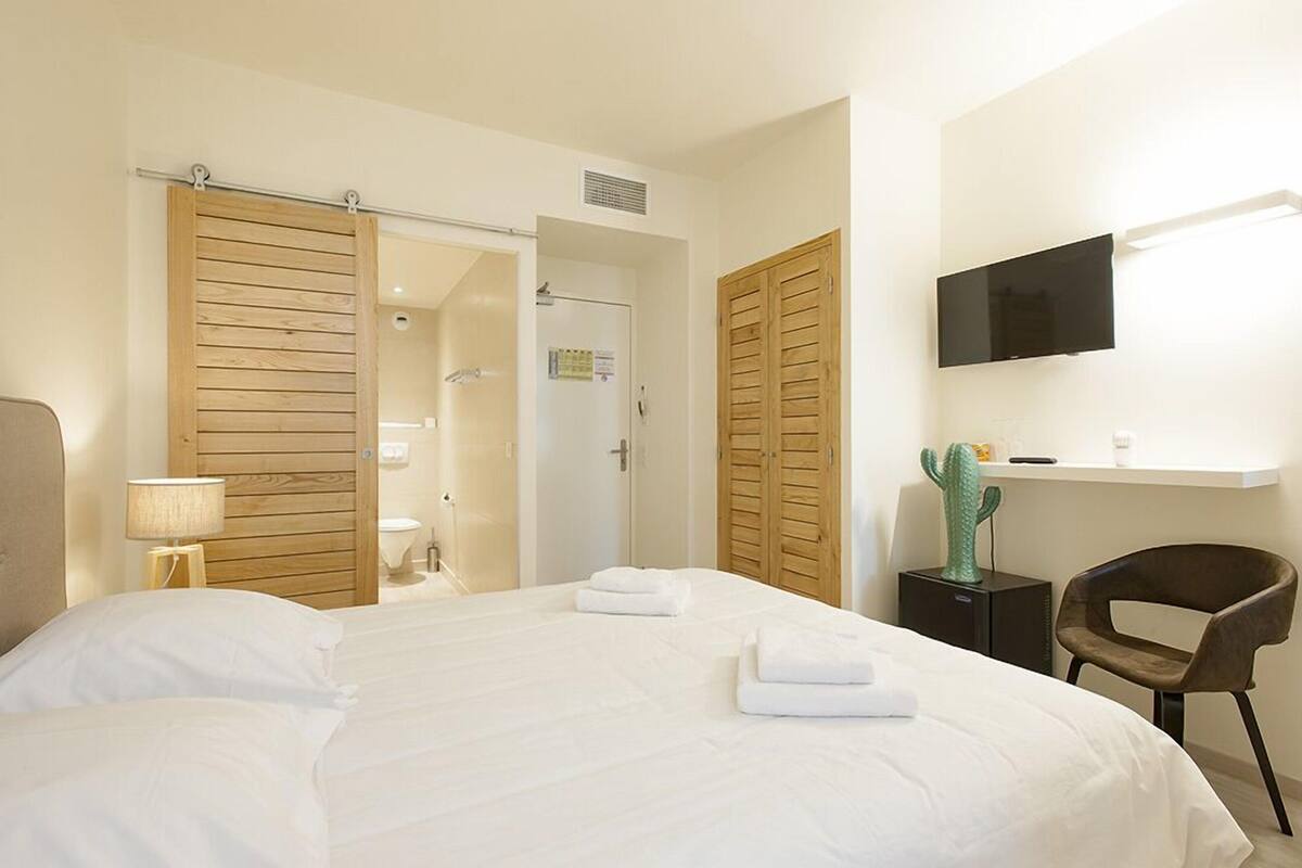A hotel room with a bed, a television mounted on the wall, a cactus decoration, and a wooden door.