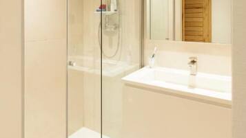 A modern bathroom with a glass-enclosed shower, a white sink, and a wooden cabinet.