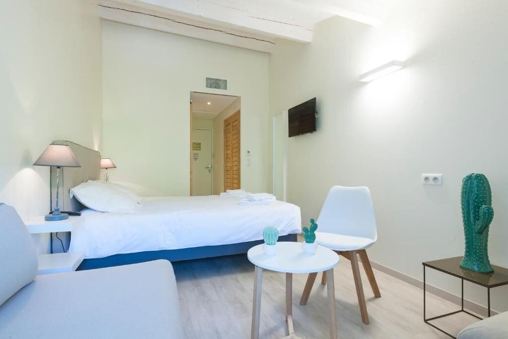 A hotel room with a bed, a desk, a chair, a small table with two cacti, and a cactus sculpture on a side table.