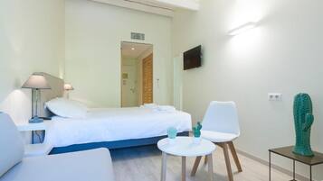 A hotel room with a bed, a desk, a chair, a small table with two cacti, and a cactus sculpture on a side table.
