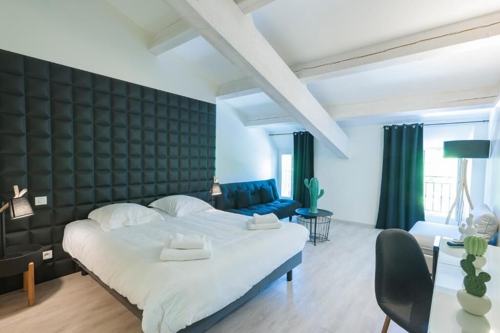 Een moderne hotelkamer met een groot bed, een blauwe bank, een cactuspunt op een tafel en een stoel.