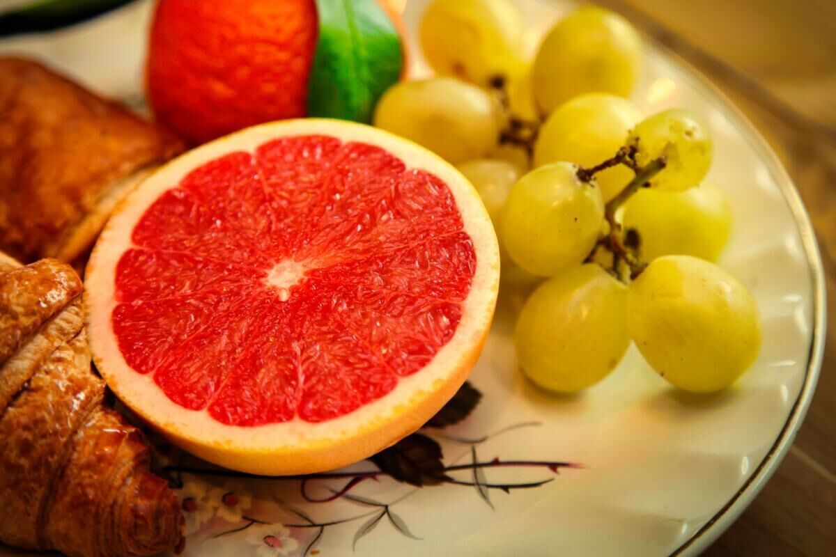 A plate with a halved grapefruit, a bunch of yellow grapes, and a croissant.