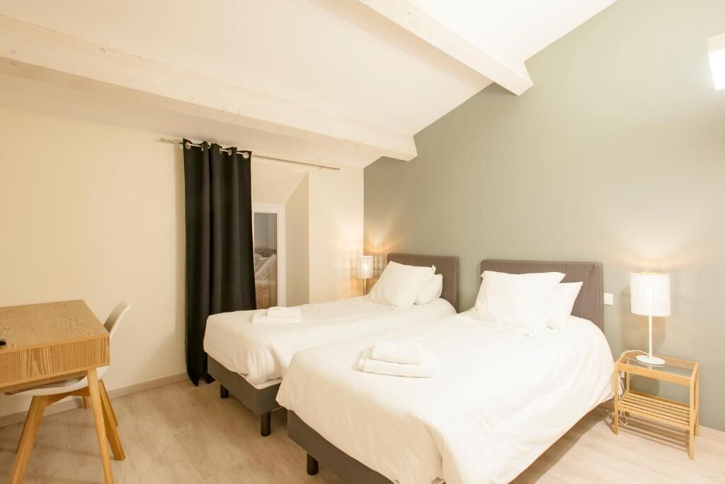 A hotel room with two beds, a wooden table, and a nightstand with a lamp.